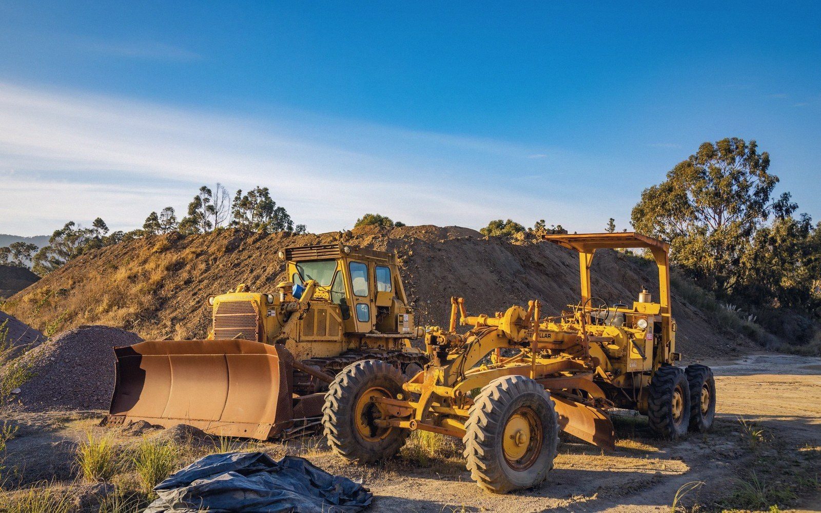 Yellow motor grader parked beside dirt mounds on a construction site