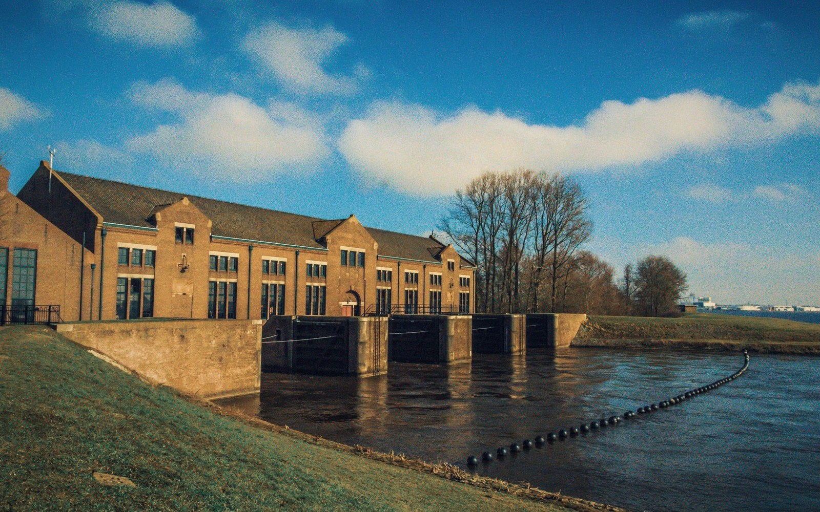 Brick pumping station with sluice gates on a riverbank under a blue sky