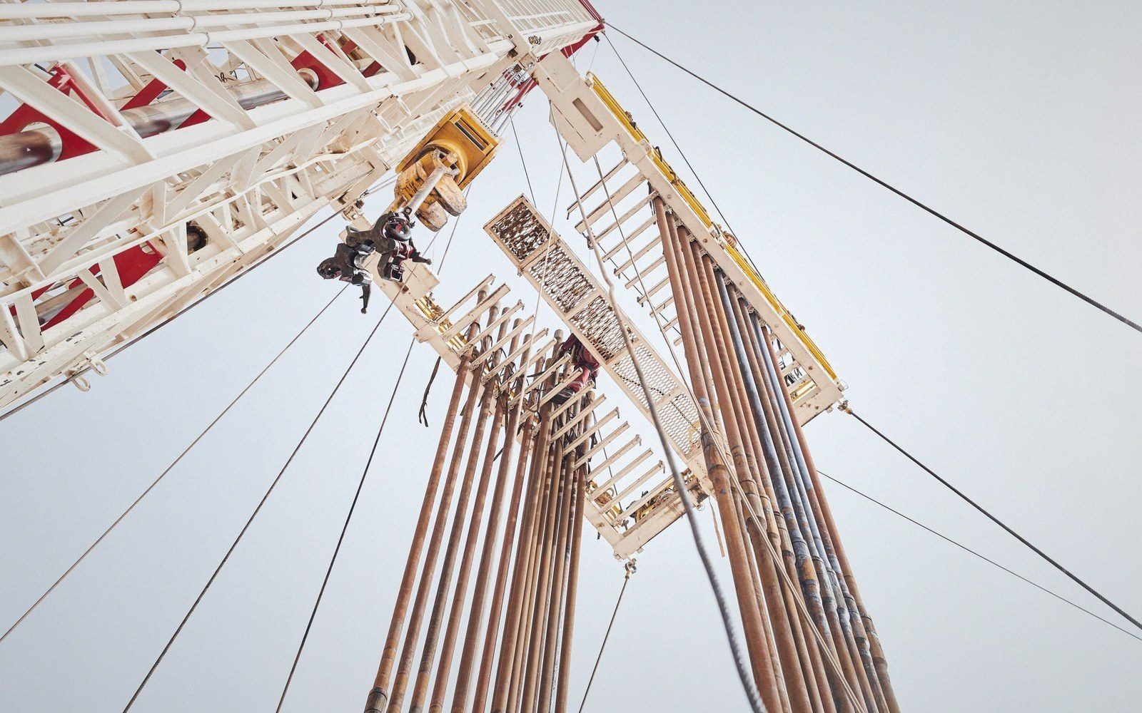 Upward view of a drilling rig derrick with stacked pipes and cables against the sky